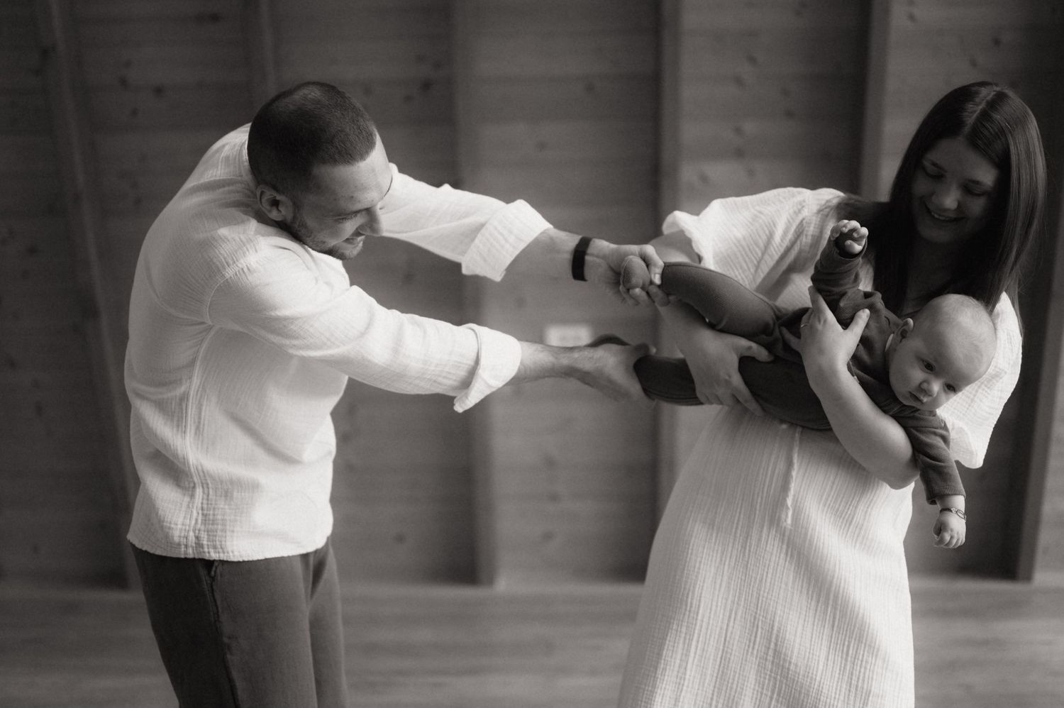 Black and white photo of parents holding their newborn baby during a family portrait session indoors.