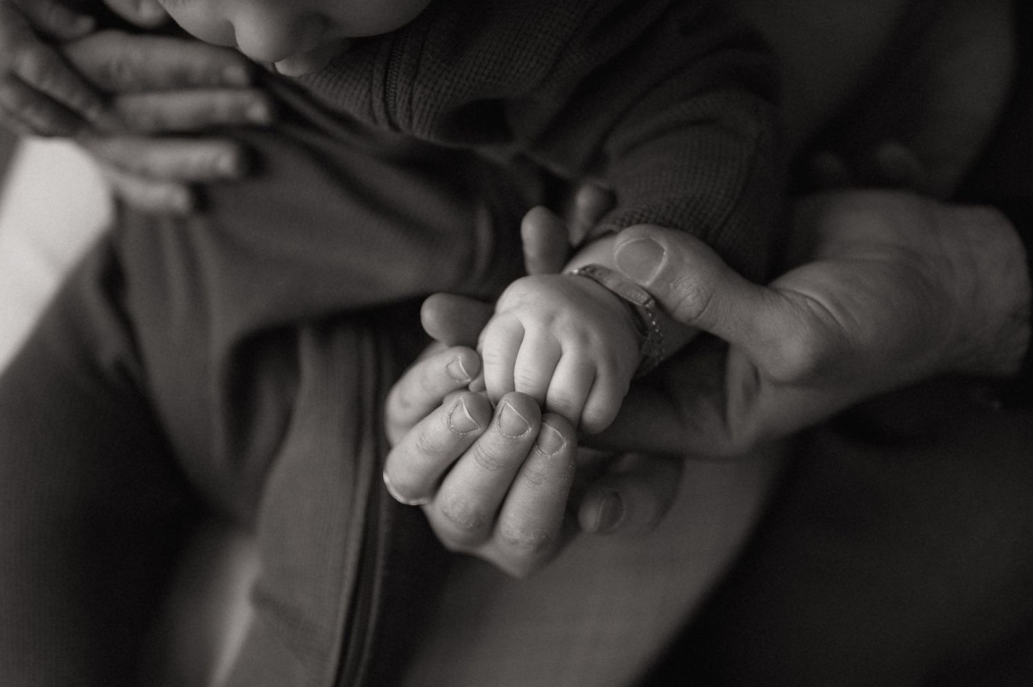 Black and white photo of an adult gently holding a newborn baby's tiny hand in a tender moment.