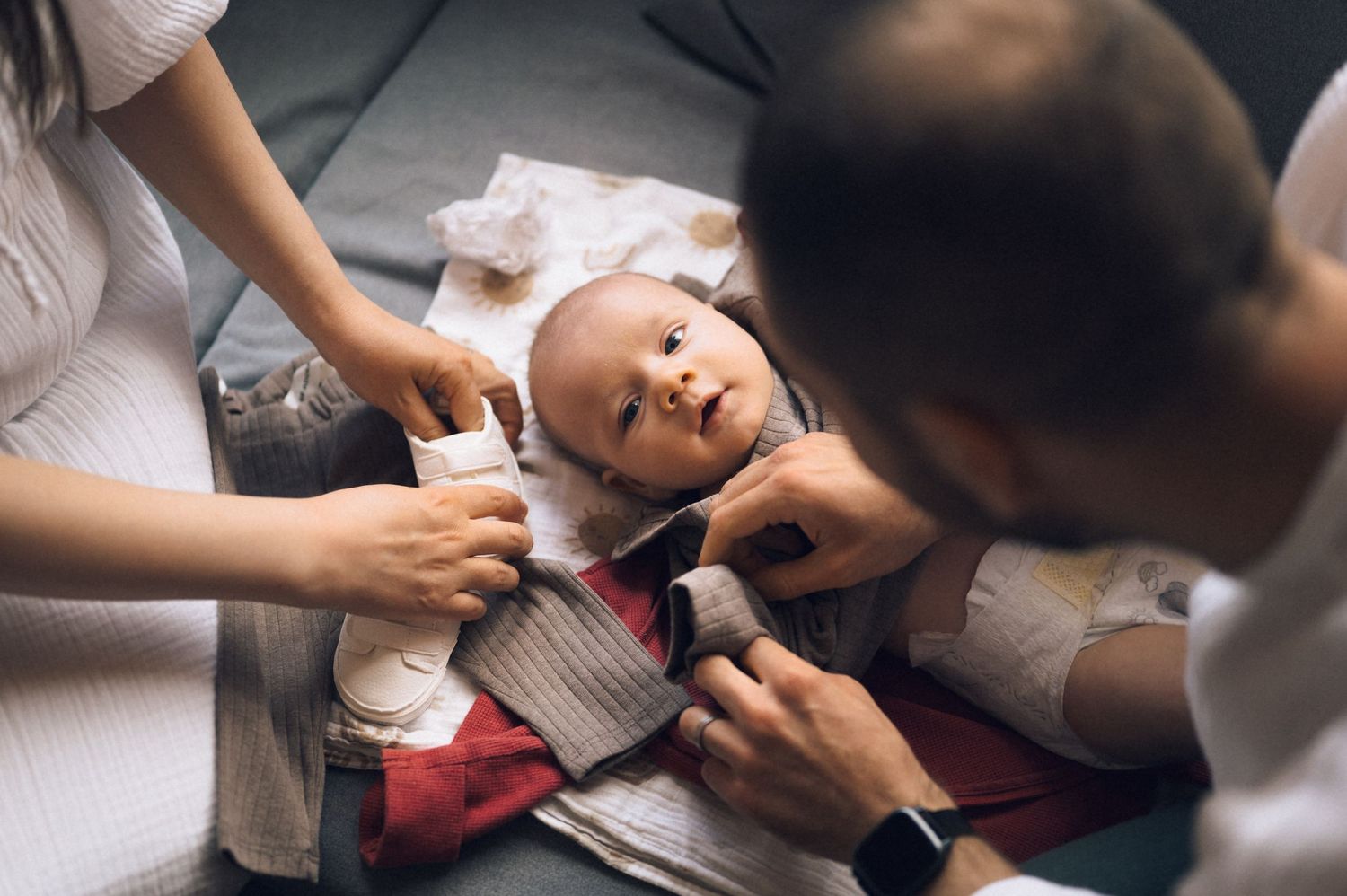 Parents dressing a newborn baby in a striped outfit while lying on a changing mat.