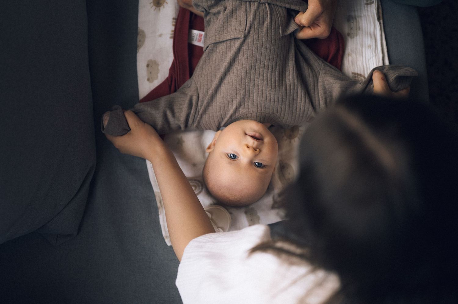 Overhead view of a young child lying on their back being playfully held by an adult caregiver indoors.