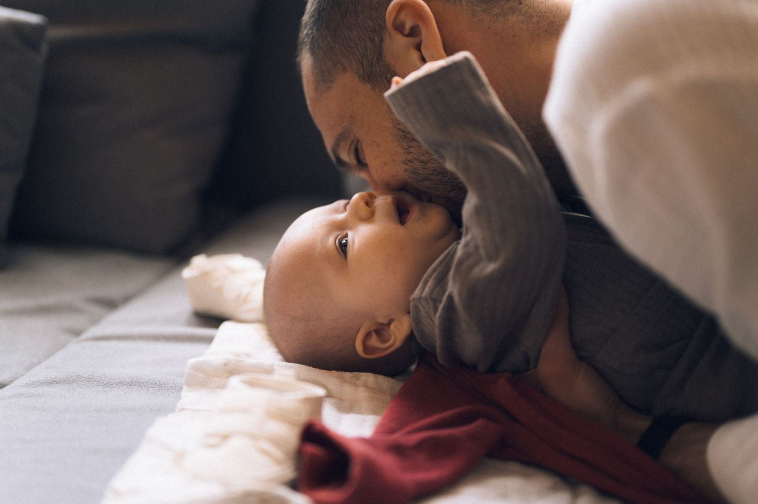 Loving father gently kissing newborn baby on couch, intimate family bonding moment.