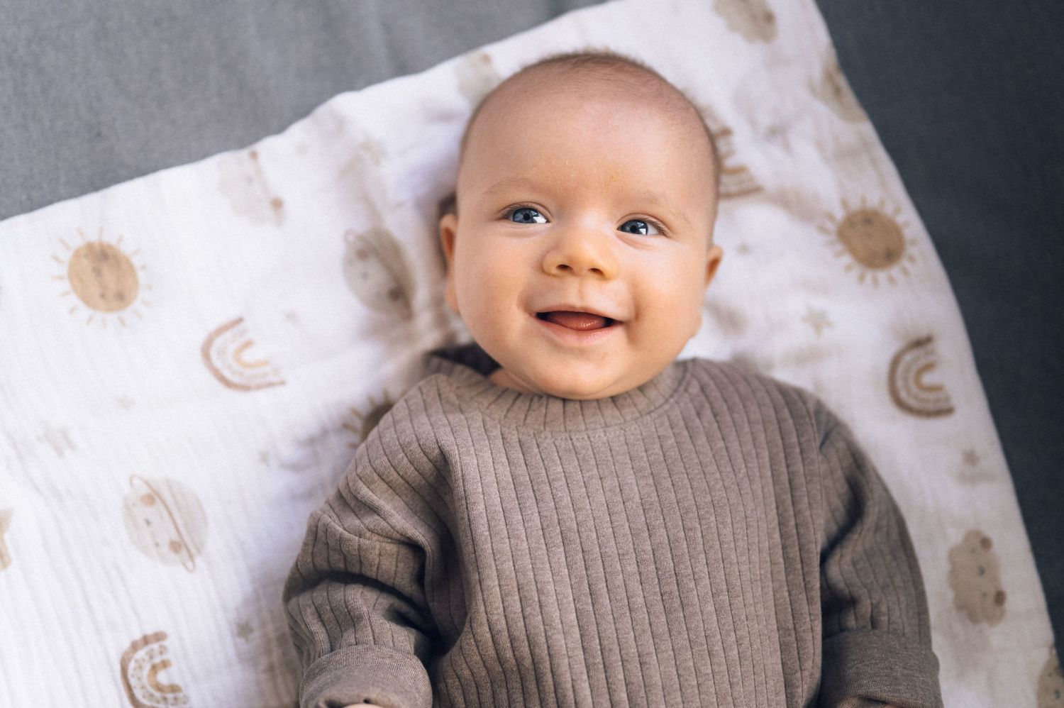 Smiling baby in a gray knit sweater lying on a celestial print blanket with suns and moons.
