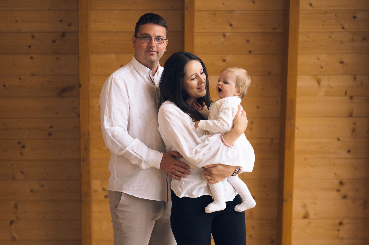 Happy young family with baby posing together in front of wooden wall background.