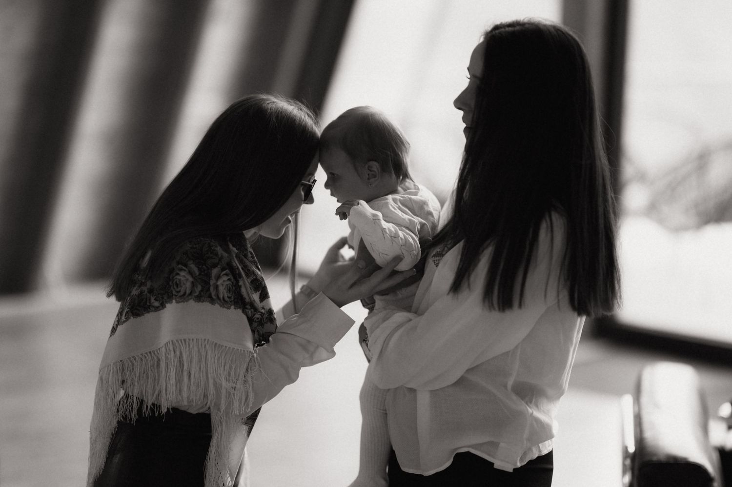 Black and white photo of two women tenderly holding a baby, sharing a heartfelt moment together indoors.