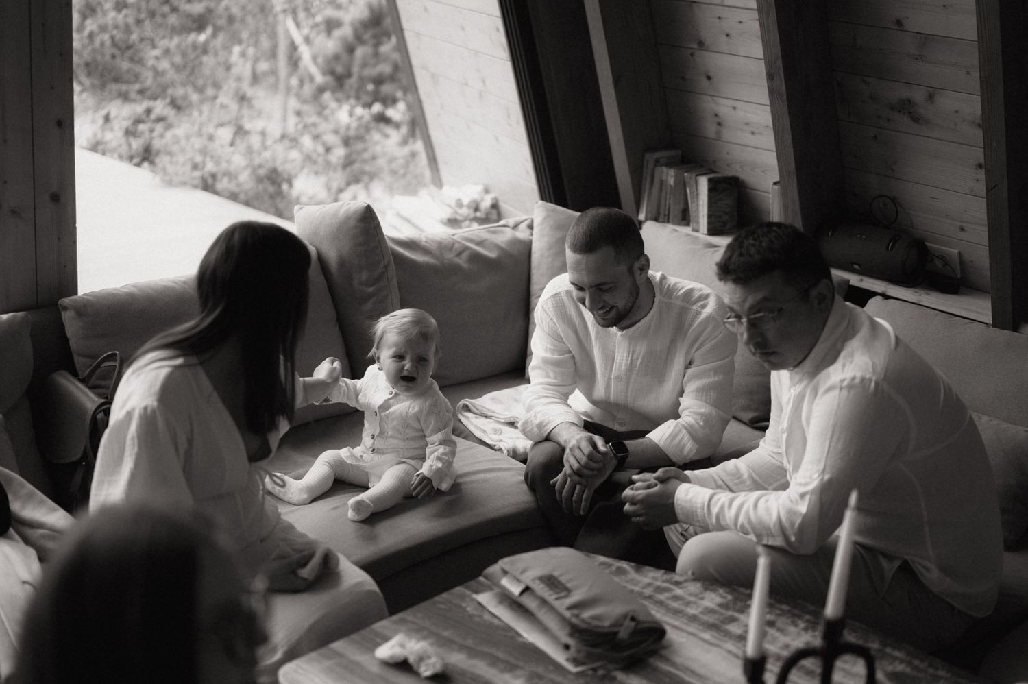 Black and white family photo of adults and a baby sitting together in a cozy cabin living room.