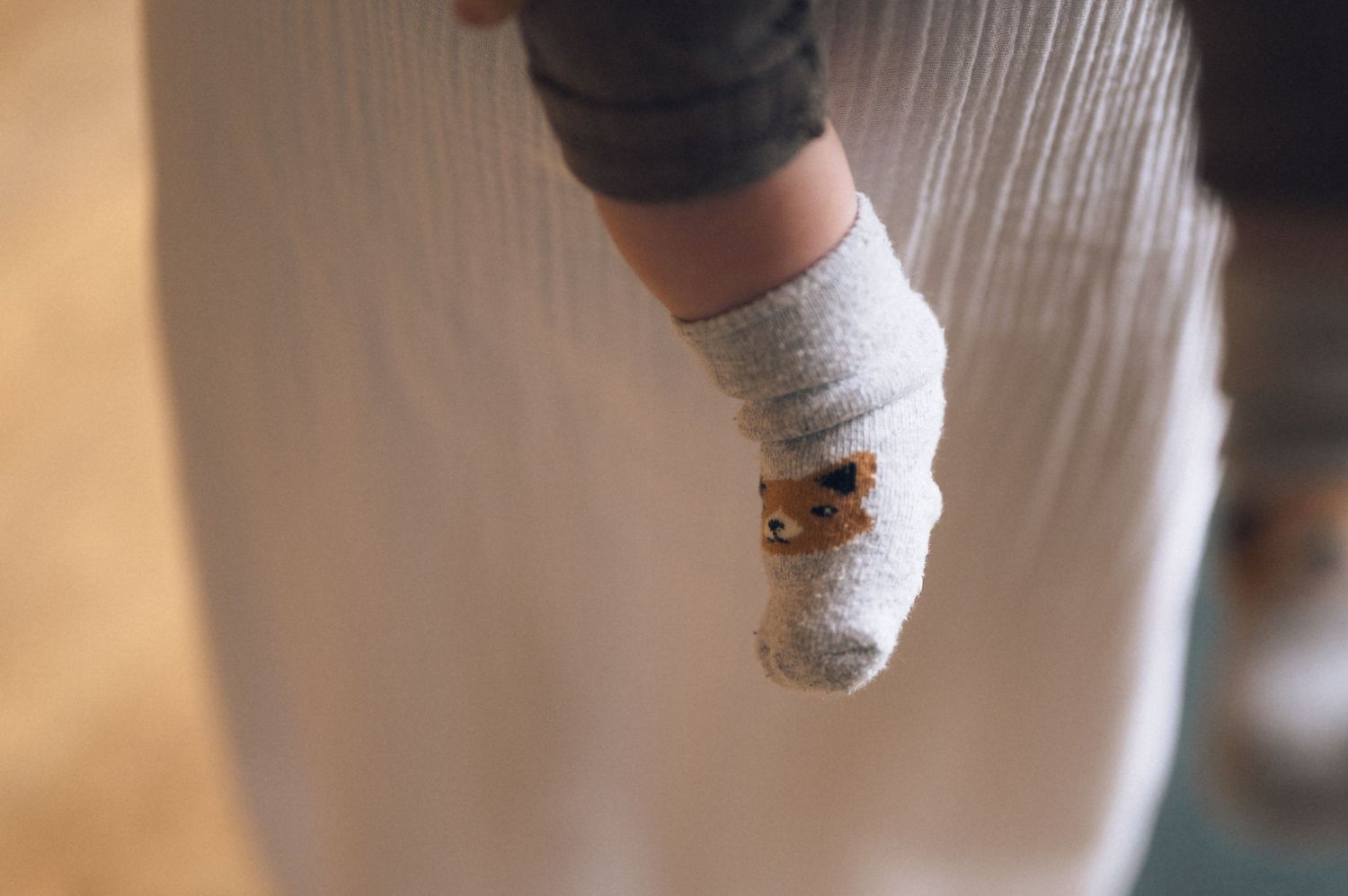Close-up of a baby's foot wearing a tiny white knit sock with a small teddy bear detail.