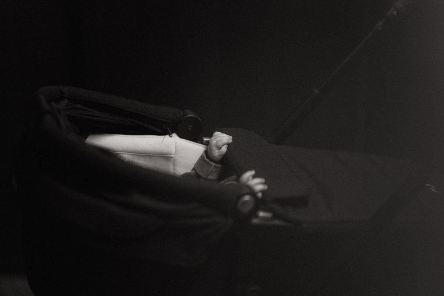 Black and white photo of a baby resting peacefully in a dark stroller or pram.