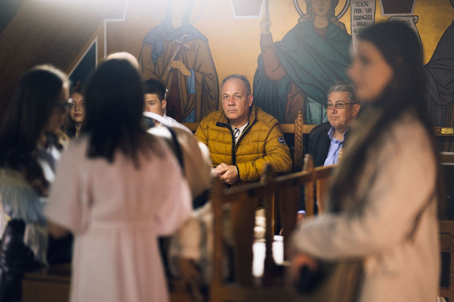 People gathered inside a church with religious icons, men seated in pews during a ceremonial service.