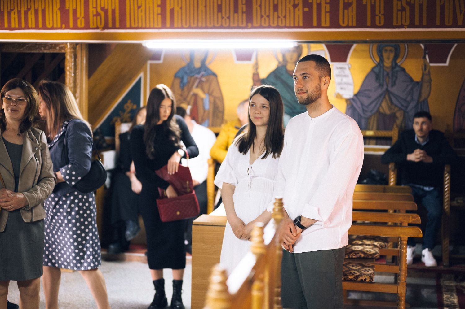Couple standing together in an Orthodox church during a religious ceremony with colorful icons on the wall.