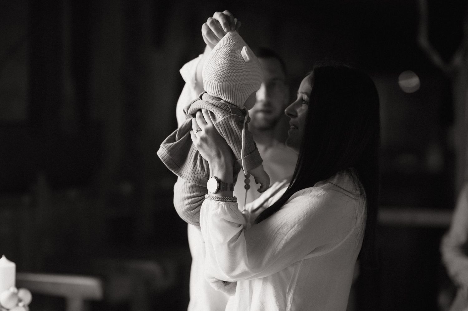 Black and white photo of a couple lovingly lifting their newborn baby in the air together.