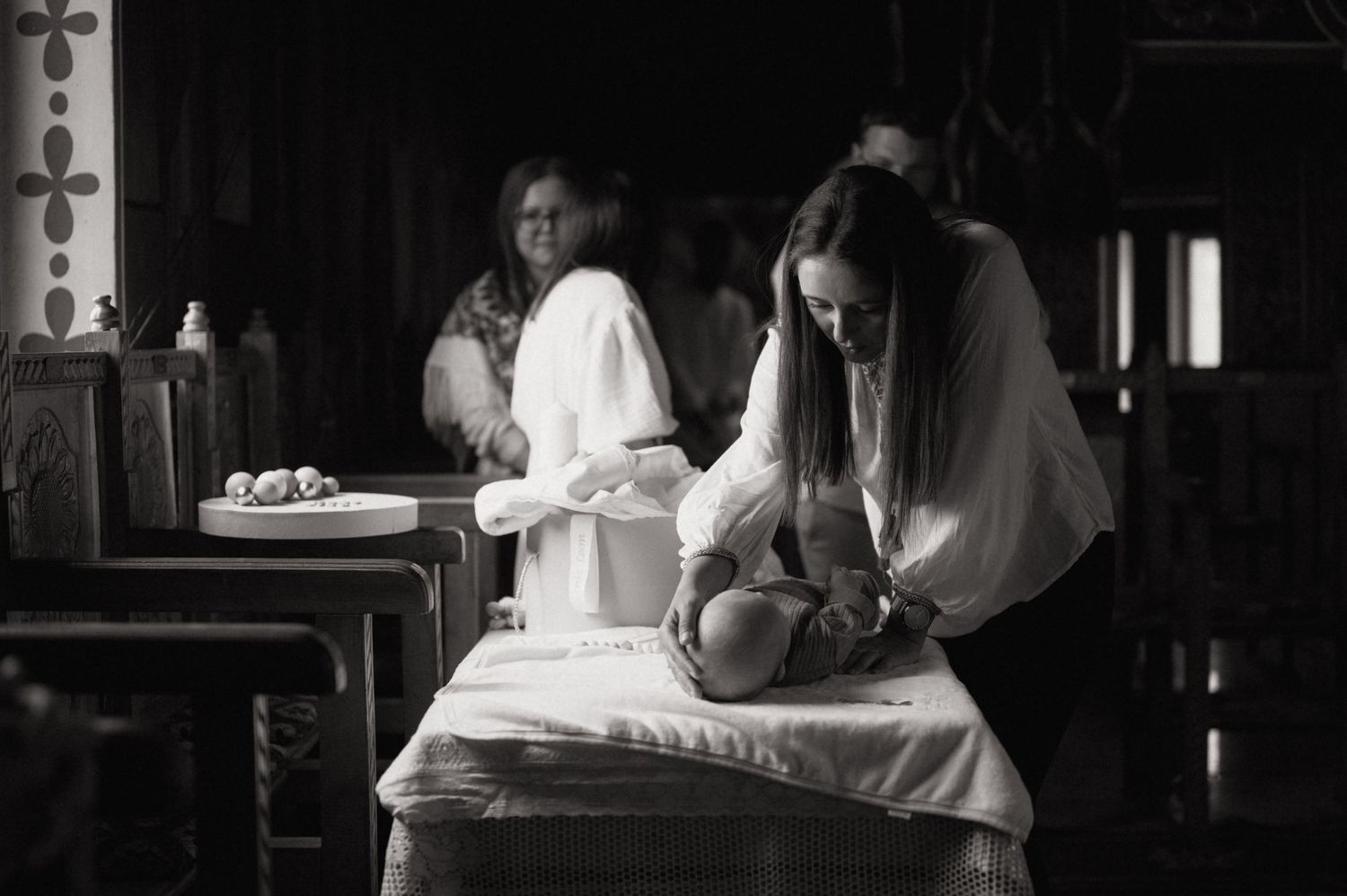 Black and white photo of a woman performing a baby baptism ceremony at a church altar.