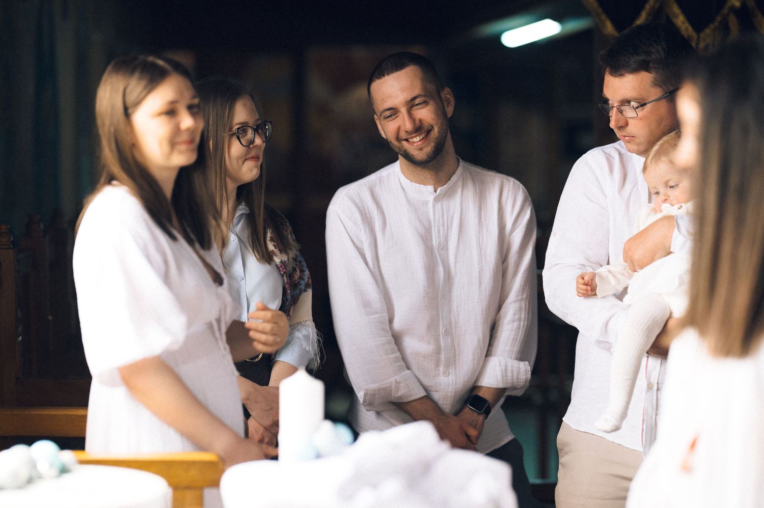 Group of young adults in white attire gathered for a baptism ceremony in a church setting.