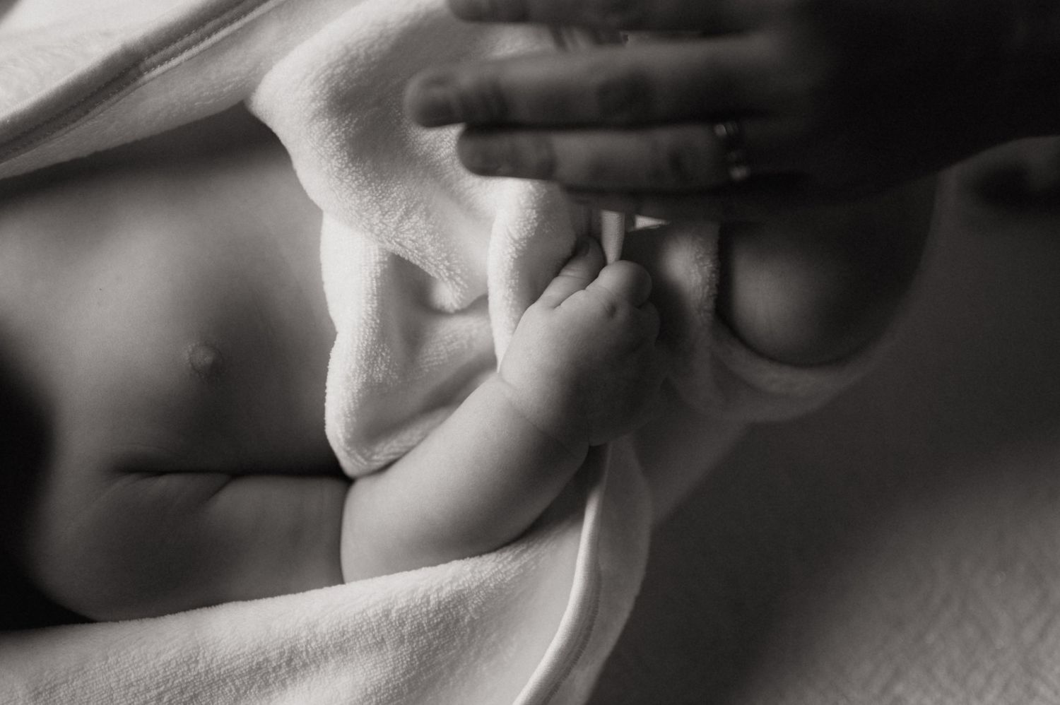 Black and white newborn baby photo with tiny feet and mother's hand on soft white blanket.
