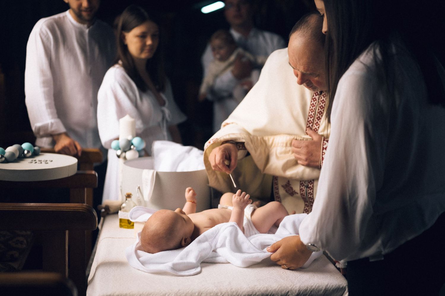 Priest performing Catholic infant baptism ceremony with baby lying on white cloth altar.