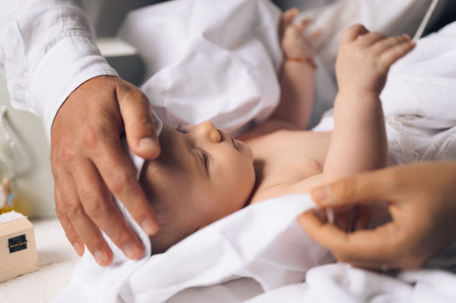 Newborn baby lying on white blanket while parents gently touch and care for the infant.