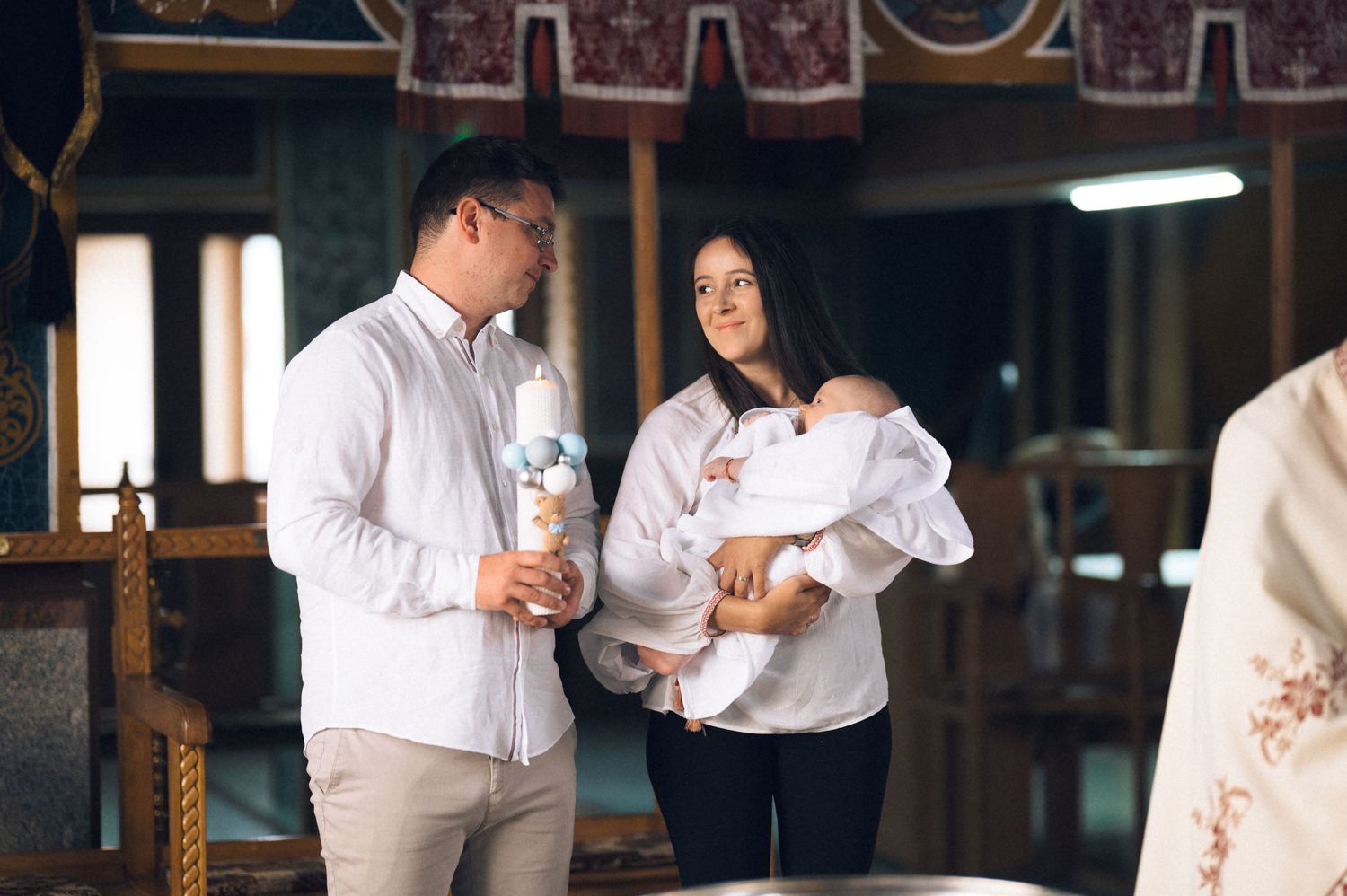 A couple holding a baby at a church baptism ceremony, with the man holding a candle.