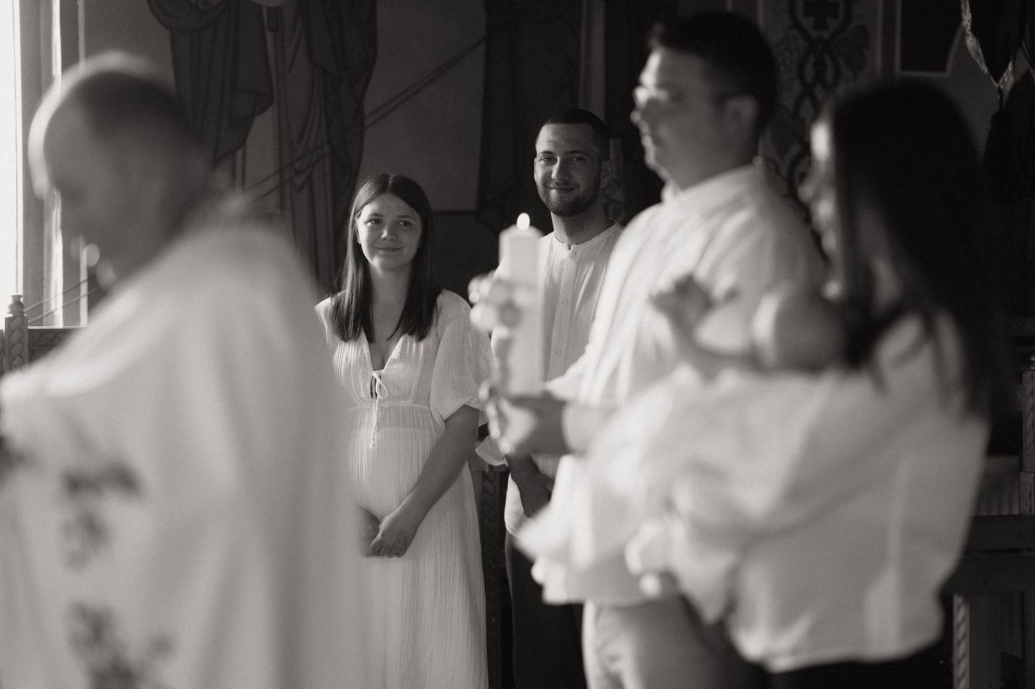 Black and white photo of guests holding candles during a religious baptism ceremony in a church.
