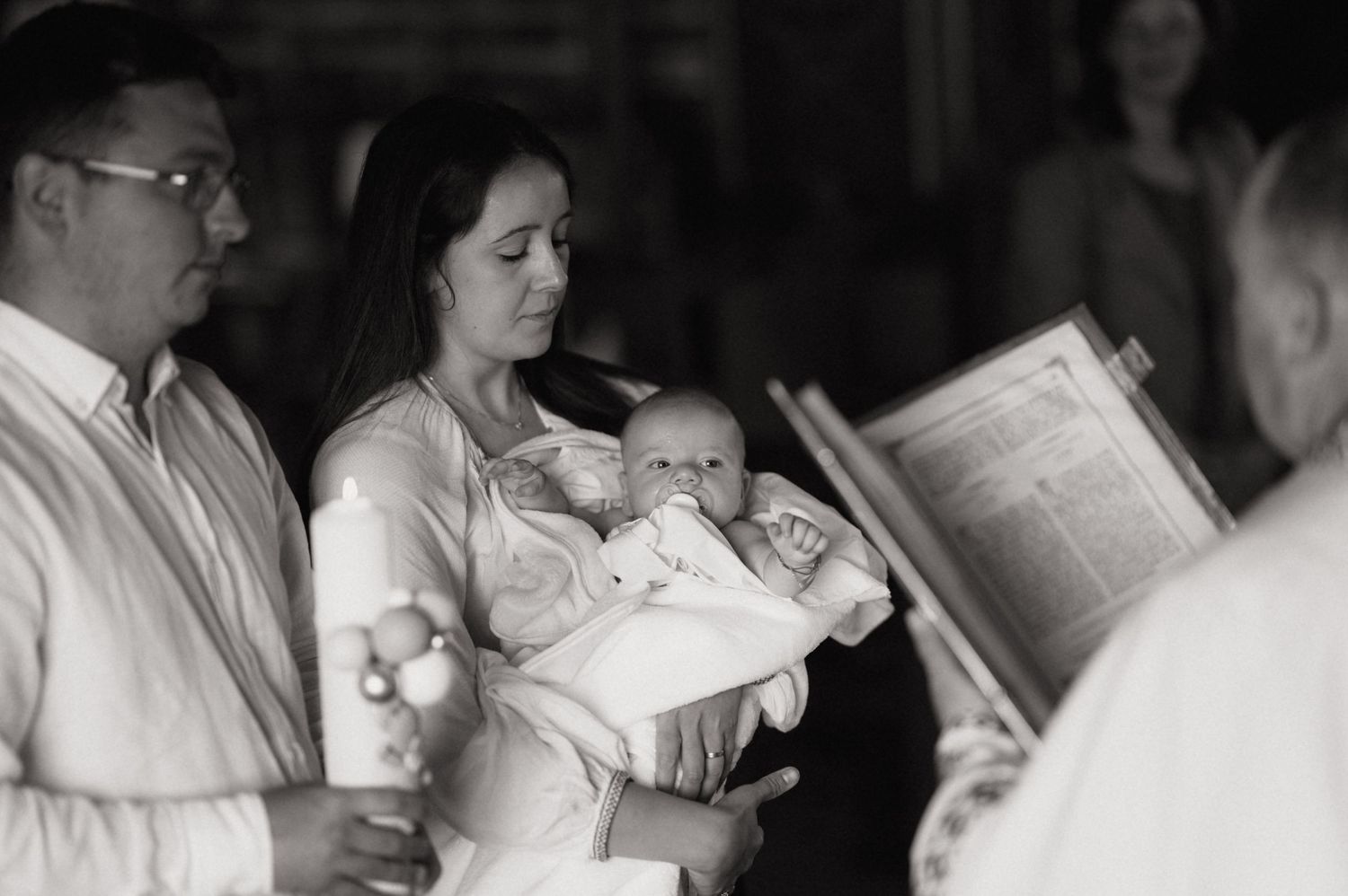 Black and white photo of a mother holding her newborn baby during a christening ceremony in a church.