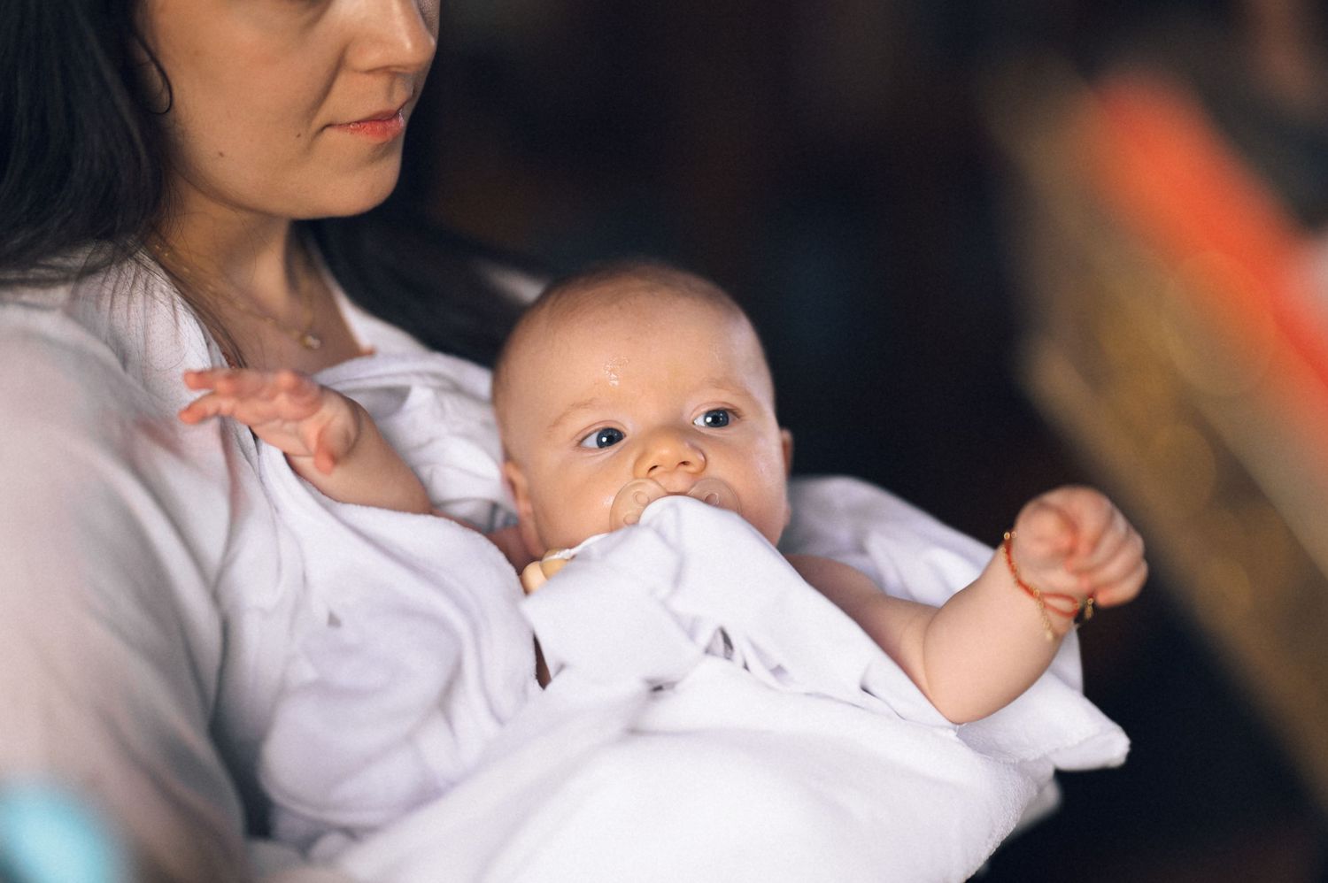A mother tenderly holds her newborn baby wrapped in a white blanket, the infant gazing curiously with bright eyes.