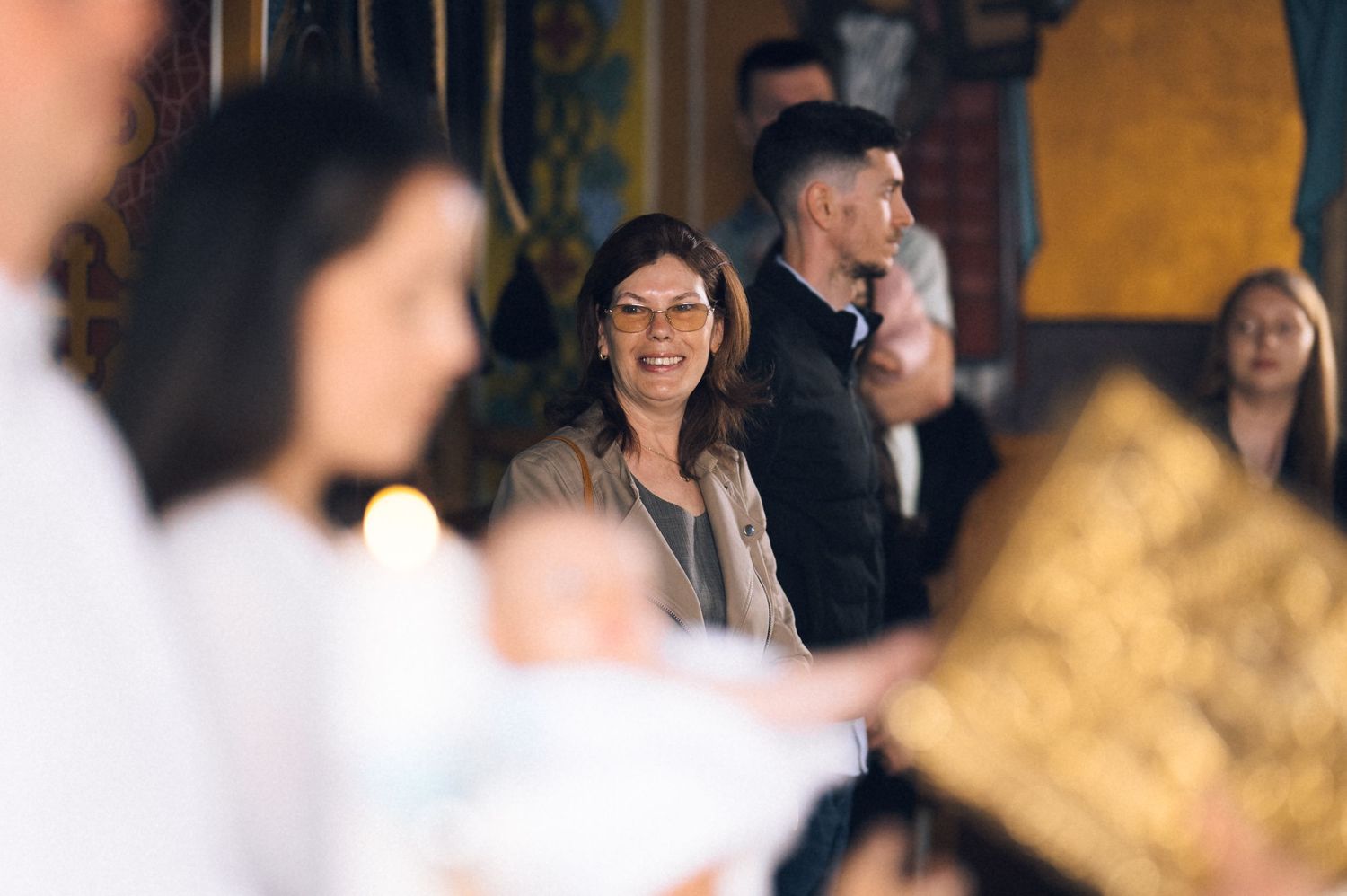 Woman smiling warmly during a church baptism ceremony with guests and golden decor in the background.