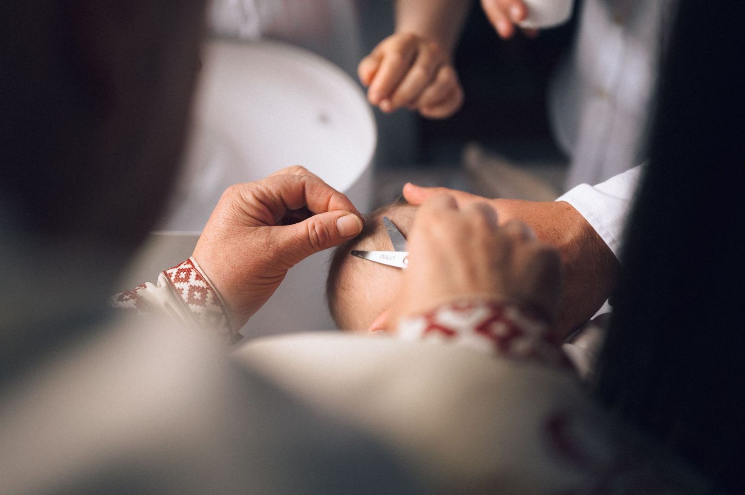 Close-up of hands fastening a cufflink on a white dress shirt with embroidered details at a wedding.