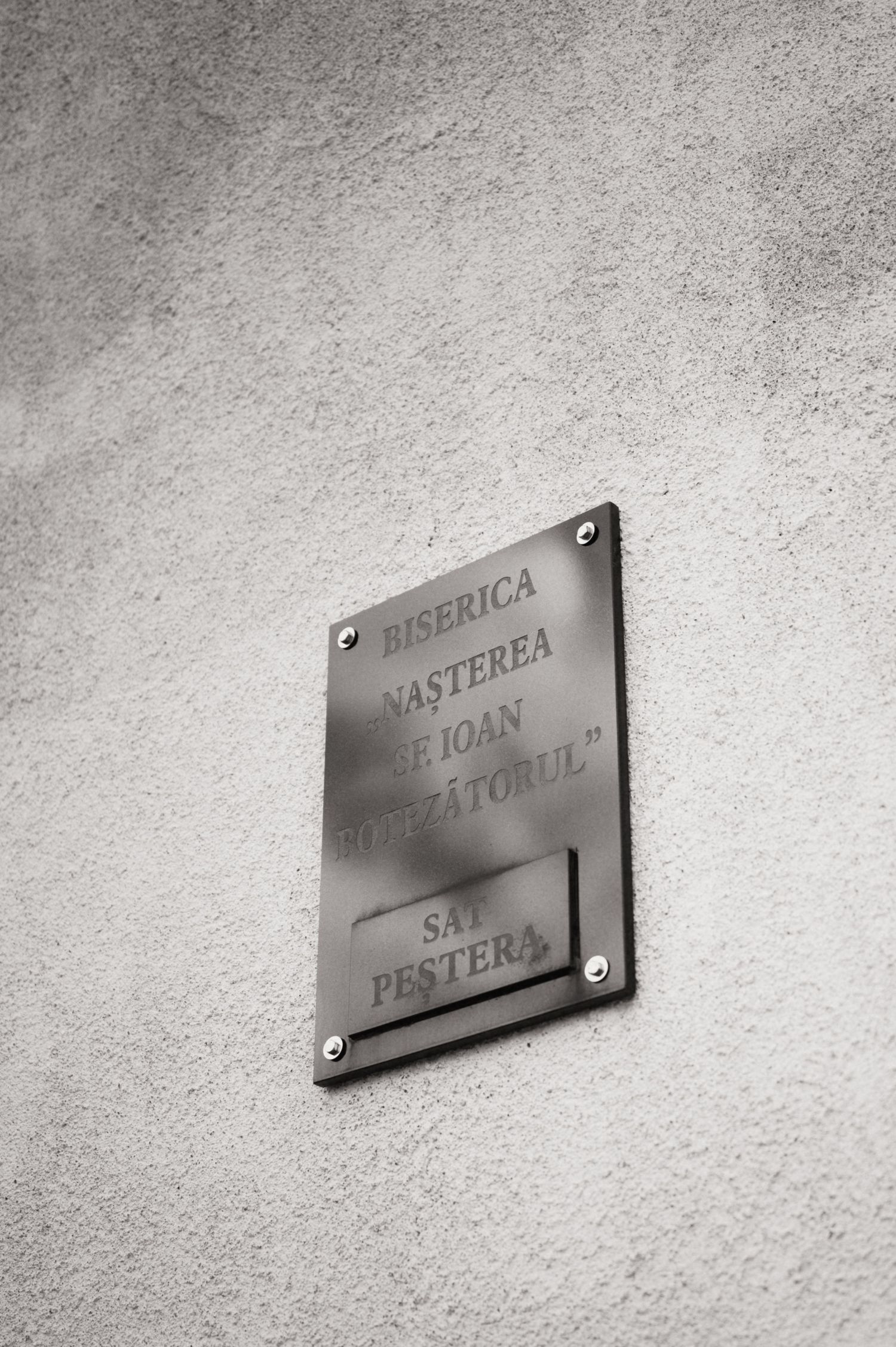 Metal plaque on a wall reading Biserica Nasterea Sf Ioan Botezatorul, Sat Pestera, Romania.