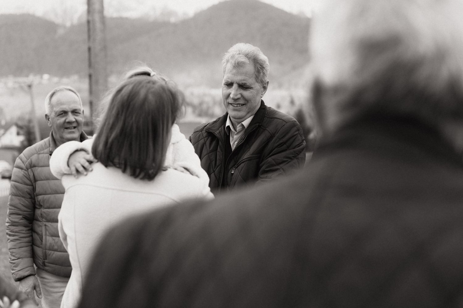 Black and white photo of smiling men socializing outdoors with mountains in the background.