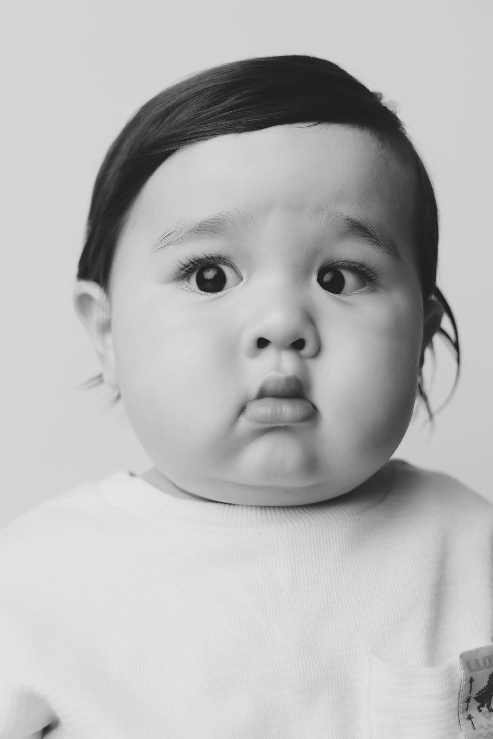 Black and white portrait of an adorable baby with chubby cheeks making a pouty face expression.