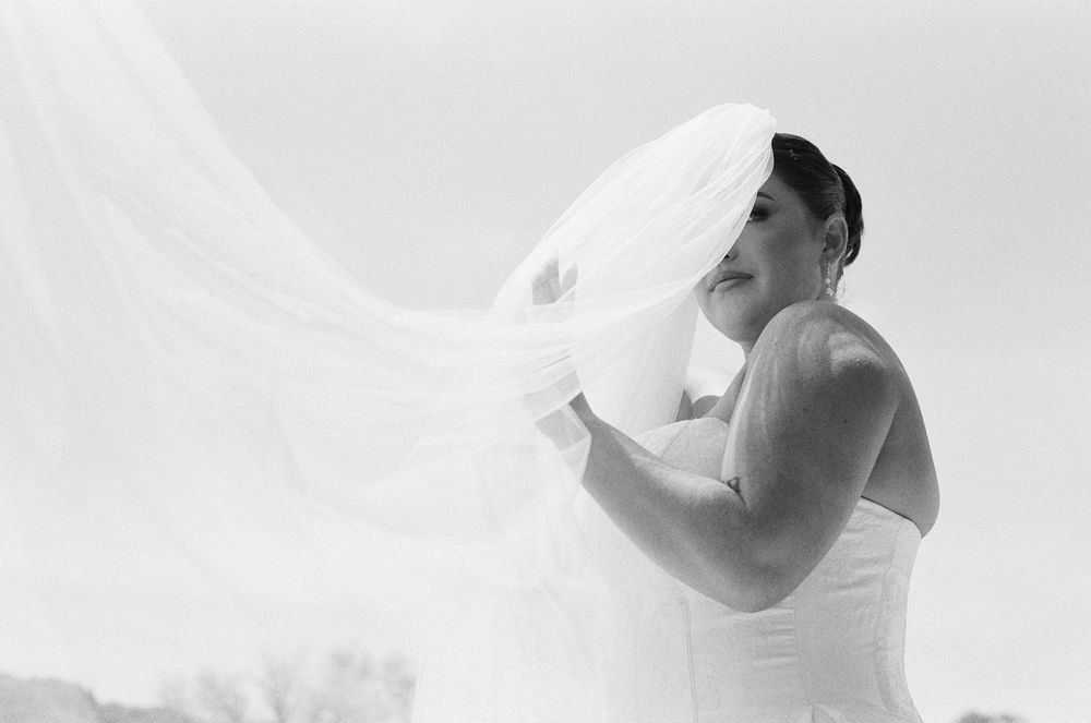 Black and white photo of a bride in a strapless gown with her veil billowing gracefully in the wind.