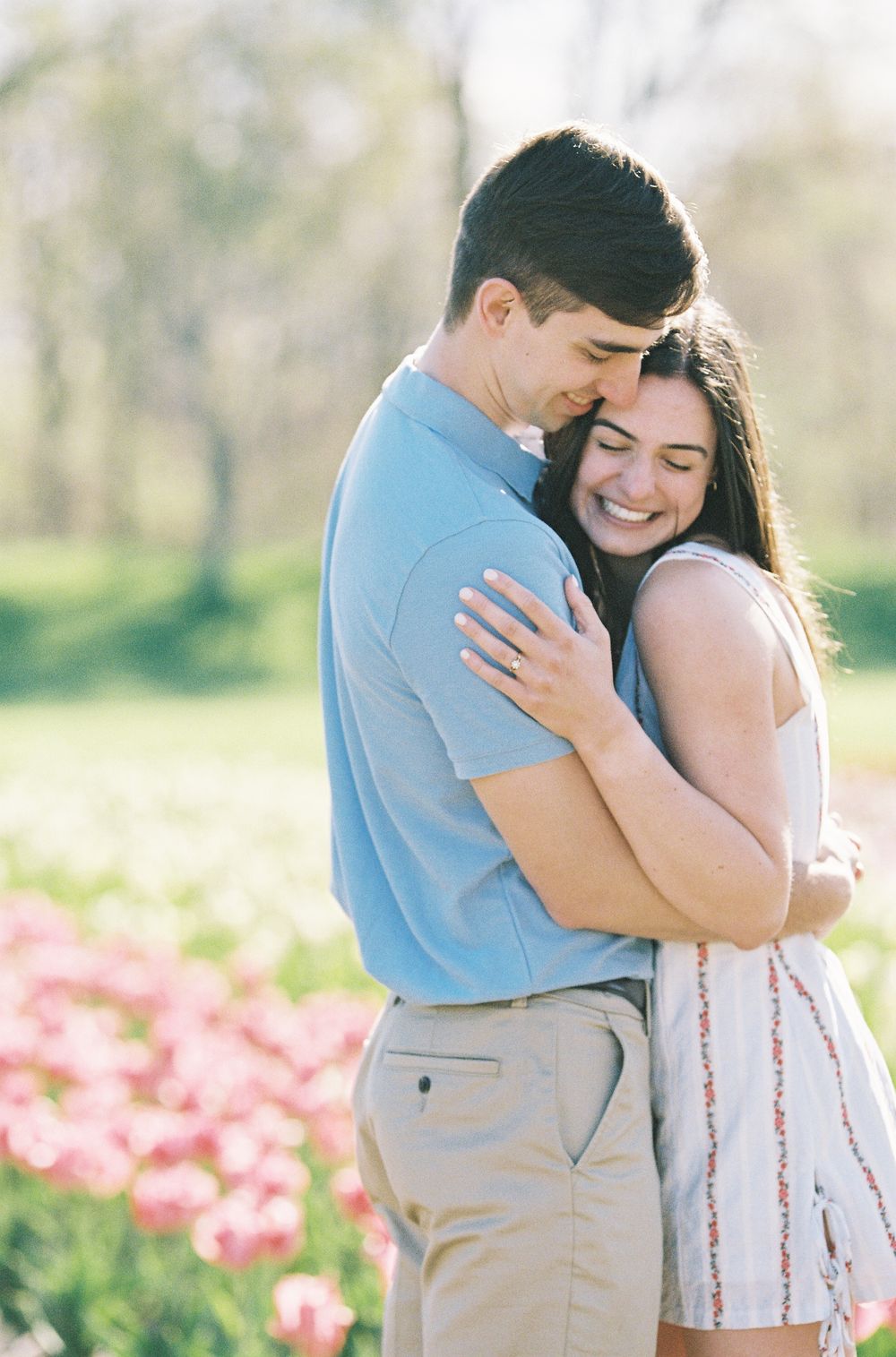 Couple embracing and smiling in a tulip field during spring engagement photo session.