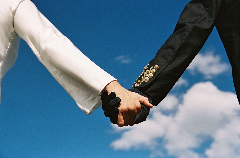 Bride and groom holding hands against blue sky, wedding couple in white and black formal attire.