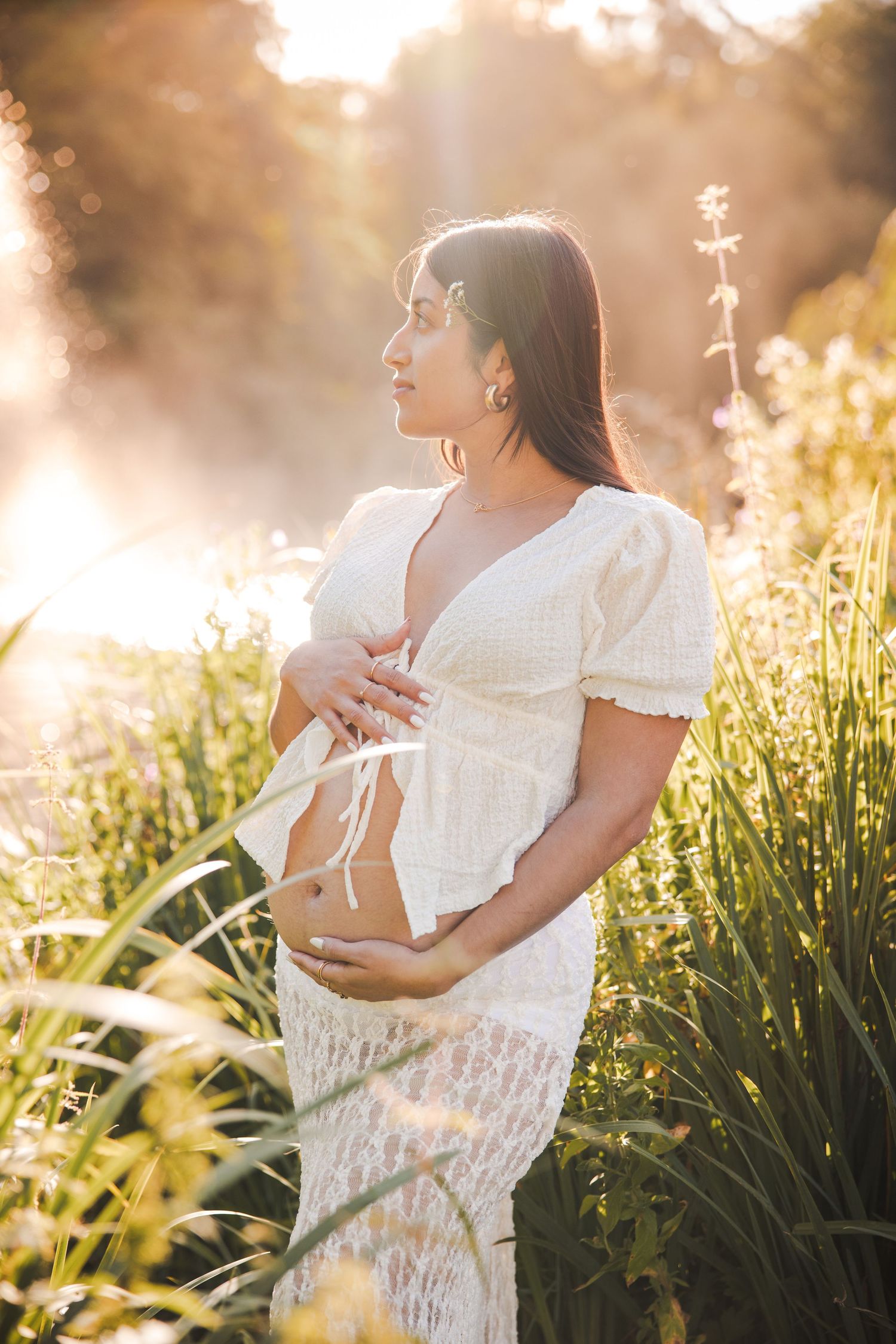 Profile of pregnant woman in white dress against a dreamy natural landscape in Vondelpark, backlit.