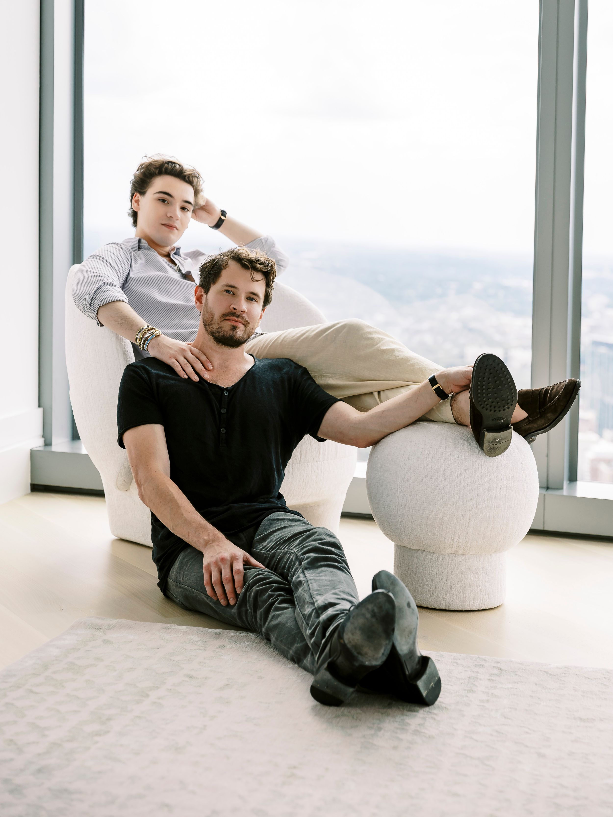 Artistic portrait series showing relaxed poses against minimalist interior with city views.