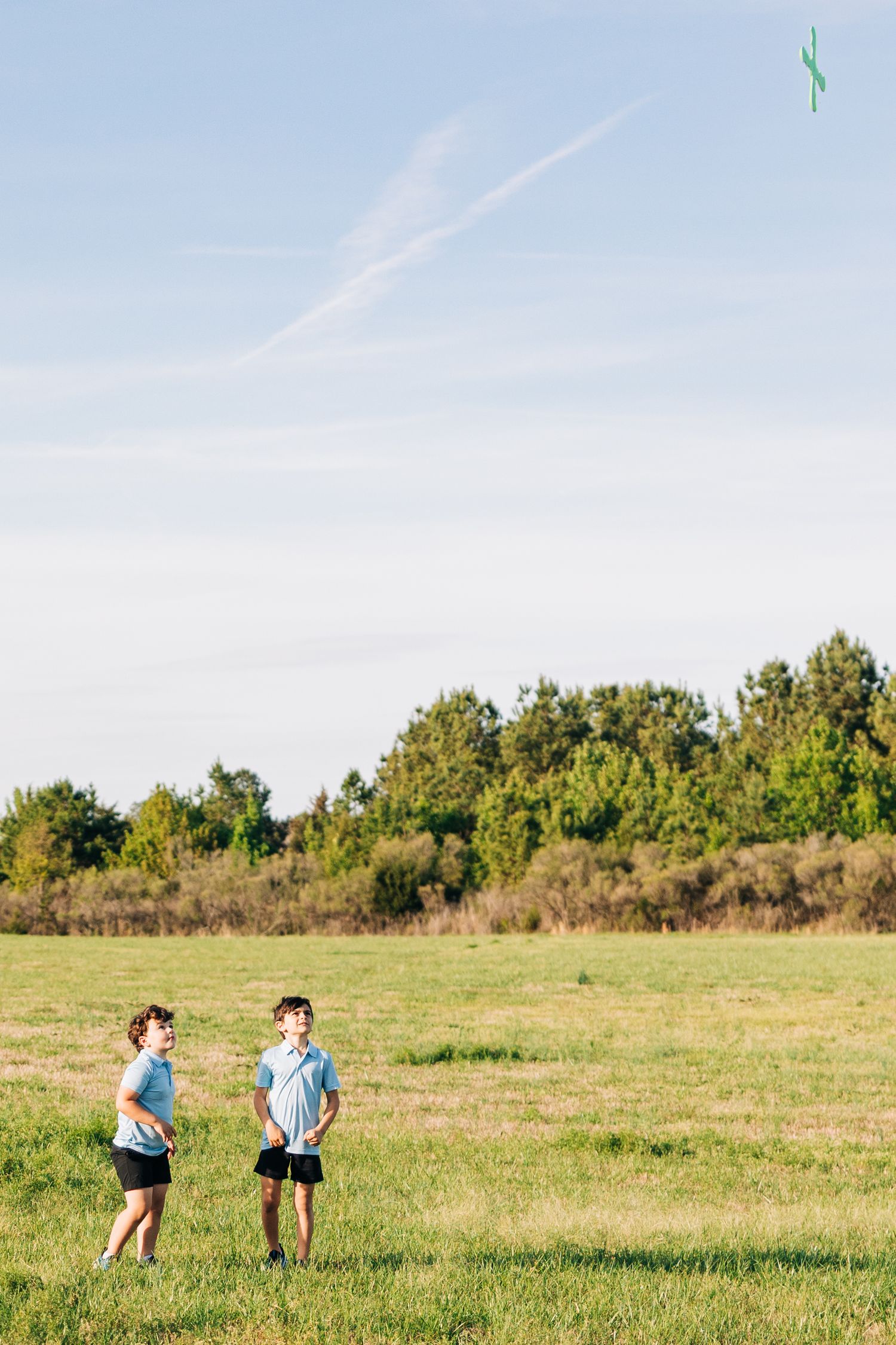 Two children chasing a boomerang in an open grassy field under a blue sky with trees in the background.