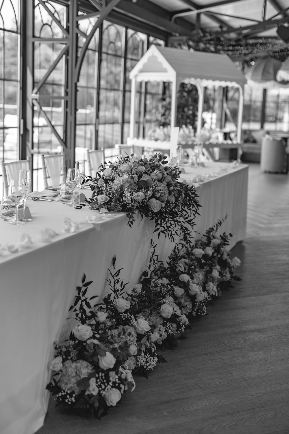 Black and white photo of floral arrangements on a wedding head table in a greenhouse venue.