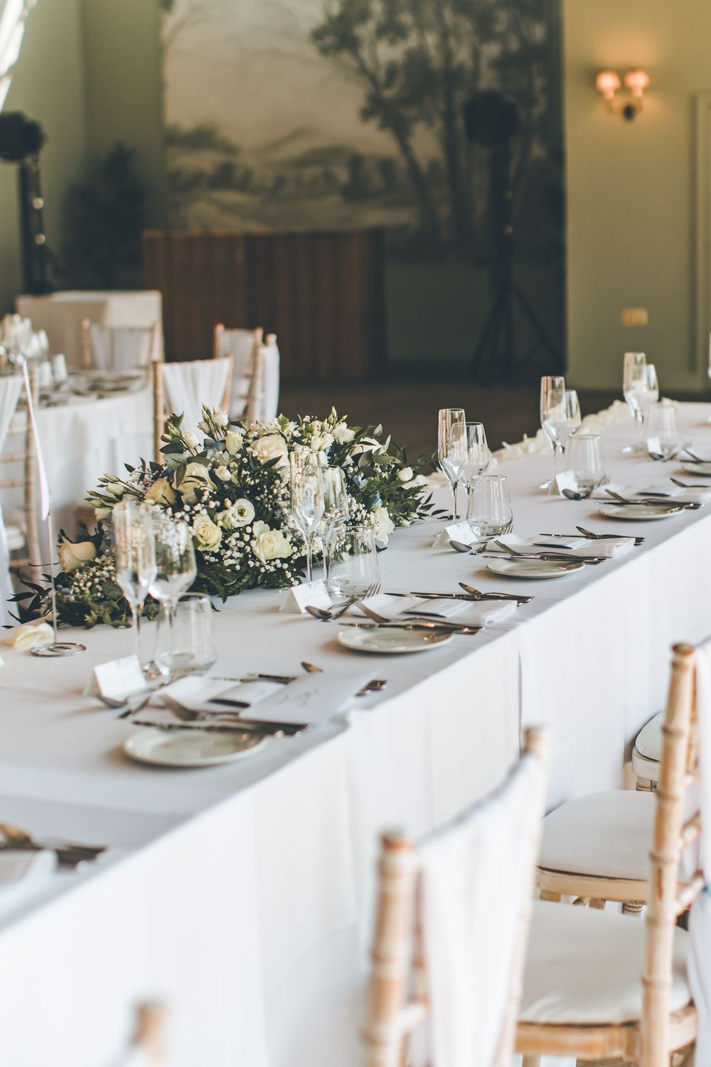 Elegant wedding reception table set with white florals, crystal glassware, and gold chairs.