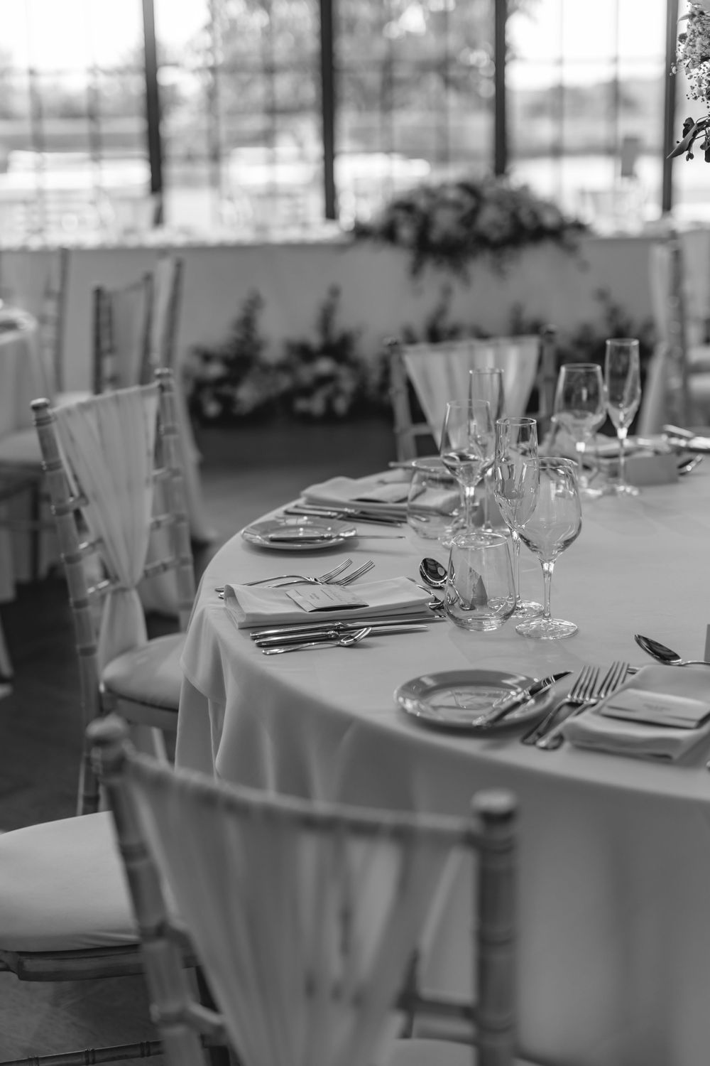 Elegant wedding reception table set with glassware, silverware, and white linens in a bright venue.