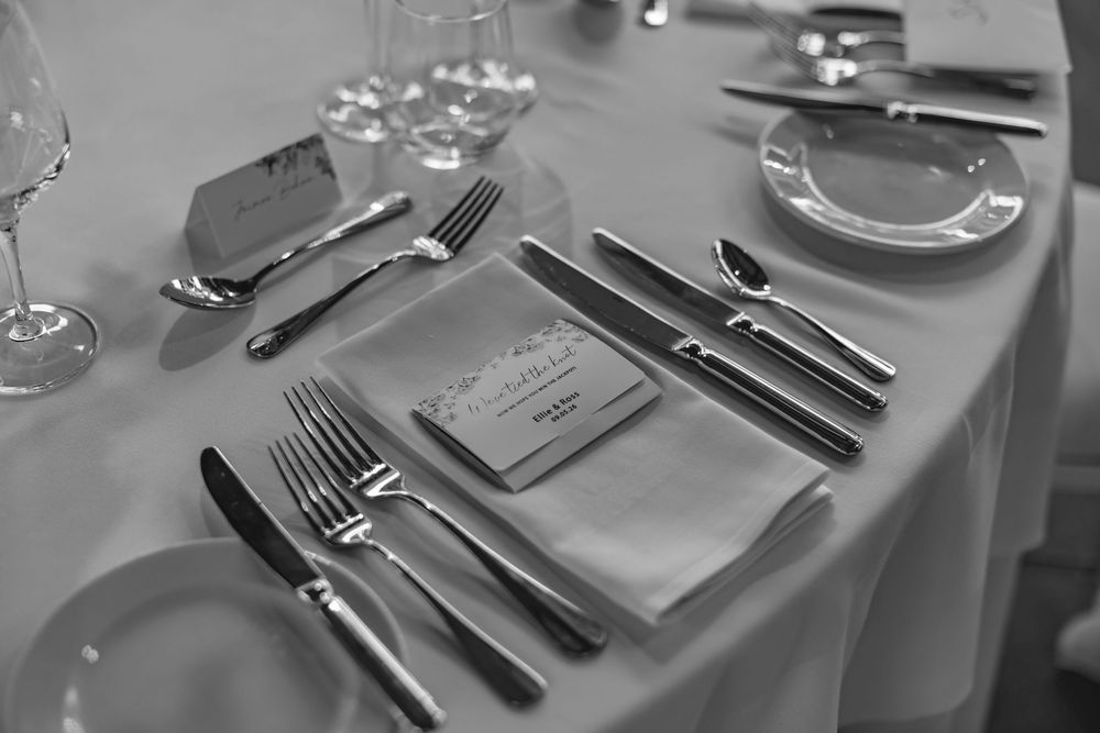 Elegant black and white wedding table setting with silverware, wine glasses, and folded napkins.
