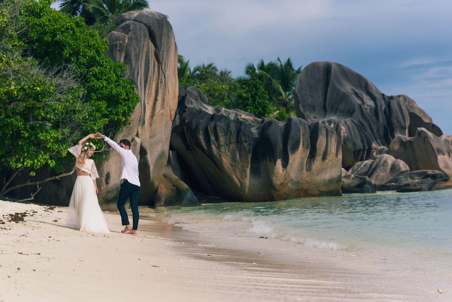 Bride and groom dancing on a tropical beach with large granite boulders and turquoise water in the Seychelles.