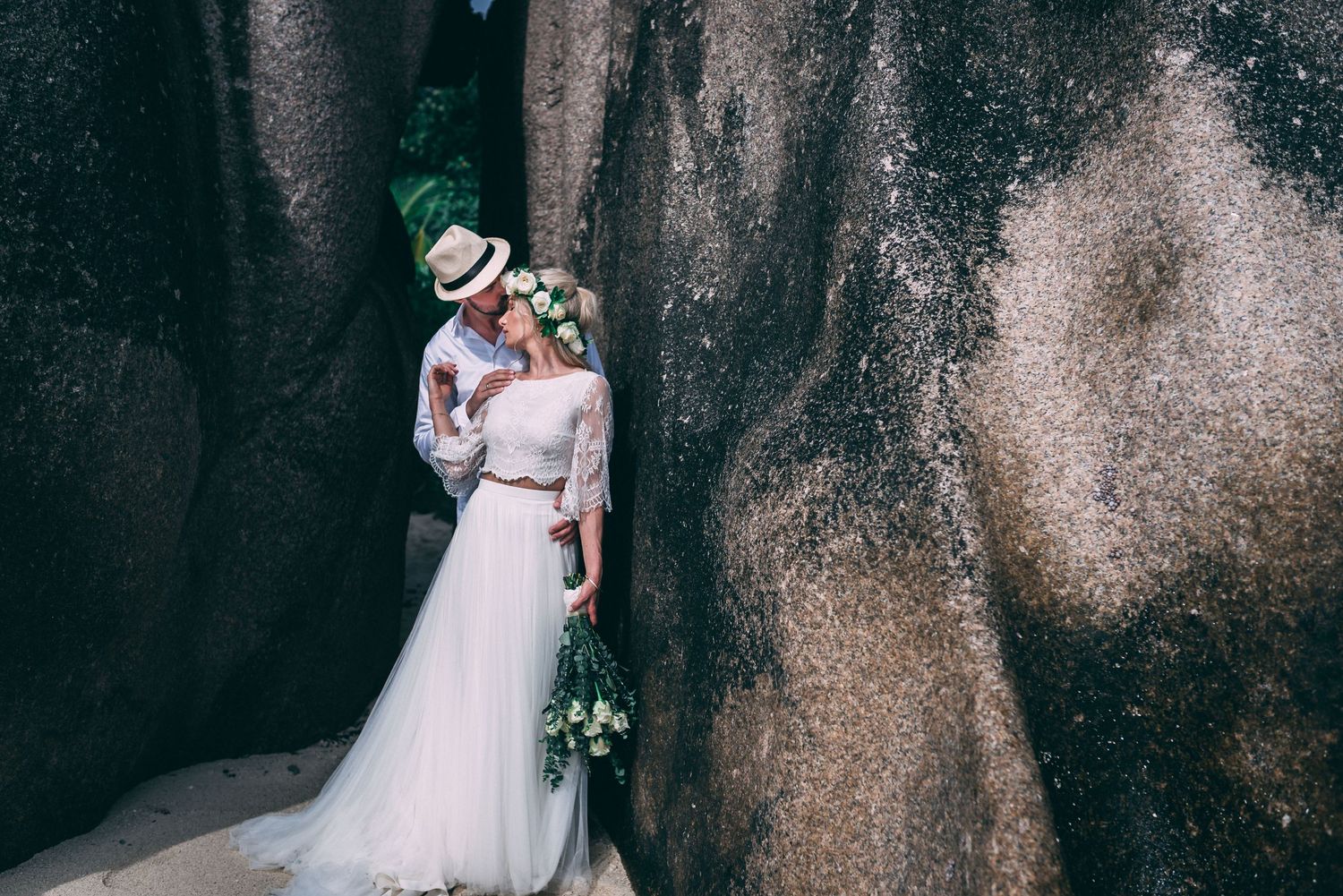 Bride and groom sharing a romantic moment between large granite rocks, bride wearing floral crown and holding bouquet.