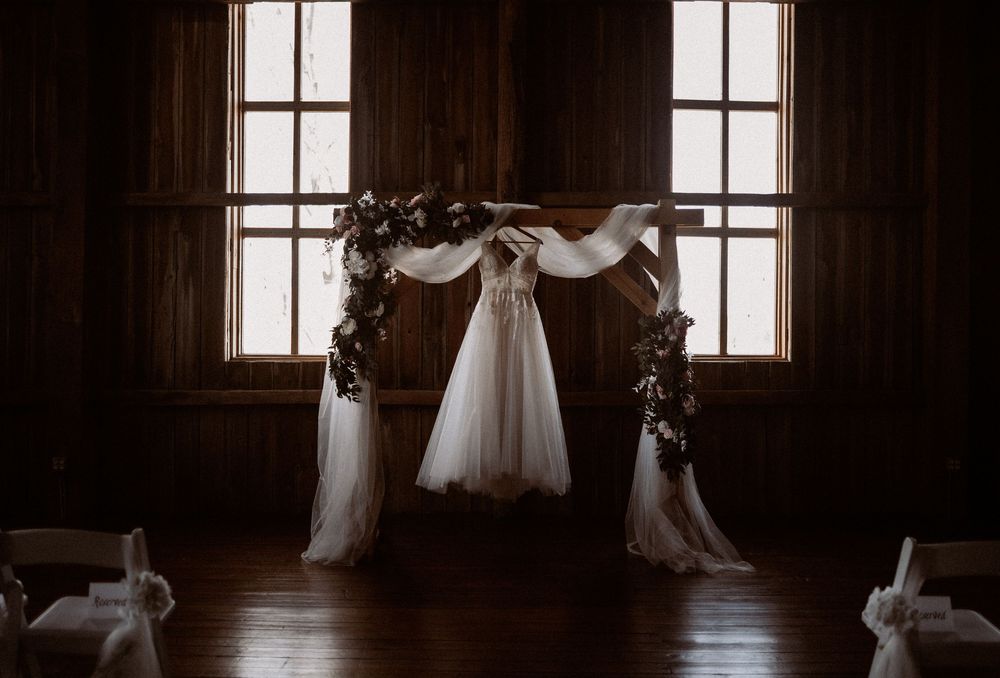 Elegant wedding arch adorned with white draping and floral arrangements inside a rustic wooden barn venue.