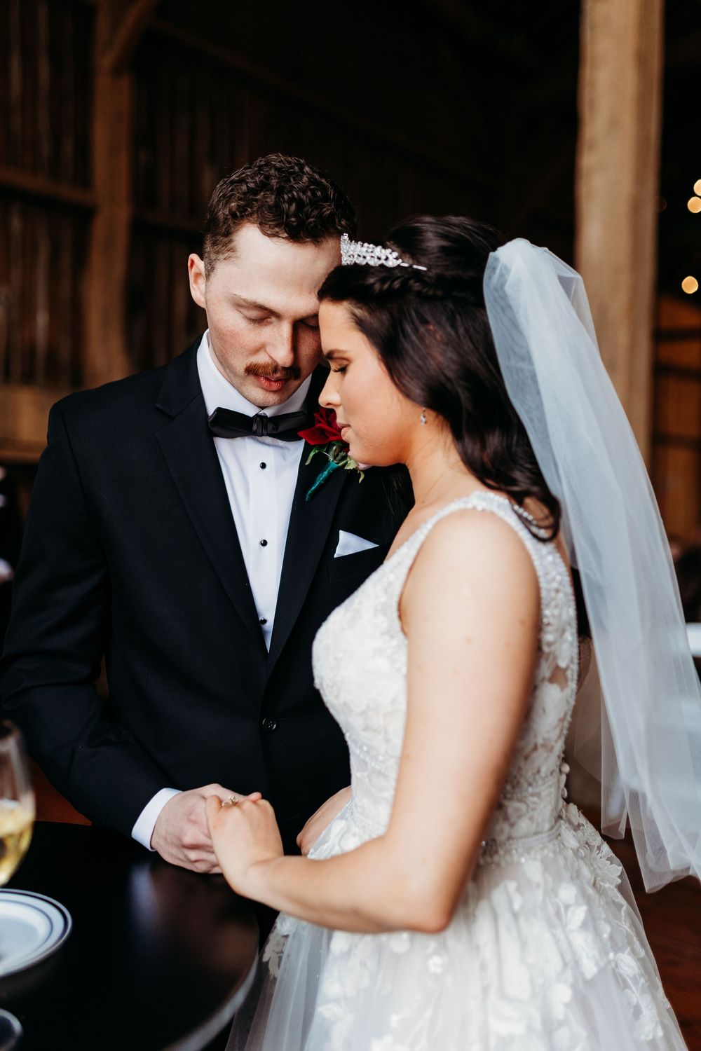 Bride and groom share an intimate moment holding hands, wearing wedding gown with tiara and black tuxedo.
