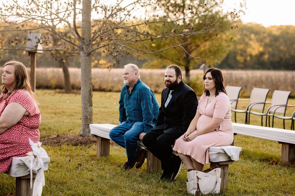 Wedding guests seated on white benches at an outdoor ceremony during golden hour on a farm.