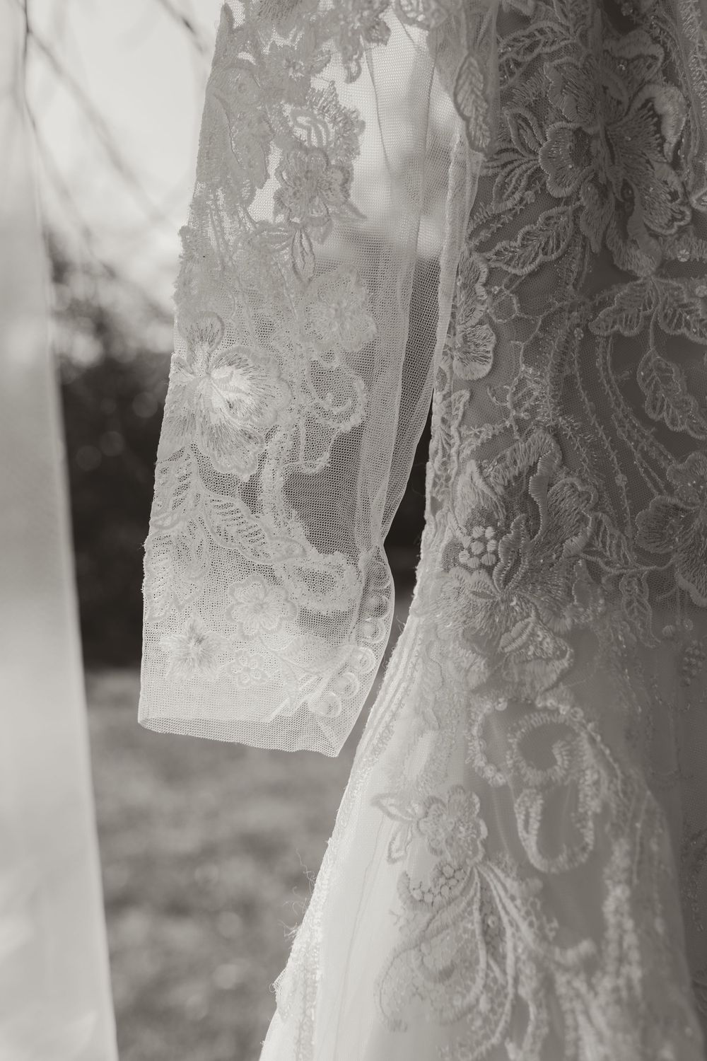 Close-up black and white photo of intricate floral lace detailing on an elegant wedding dress sleeve.