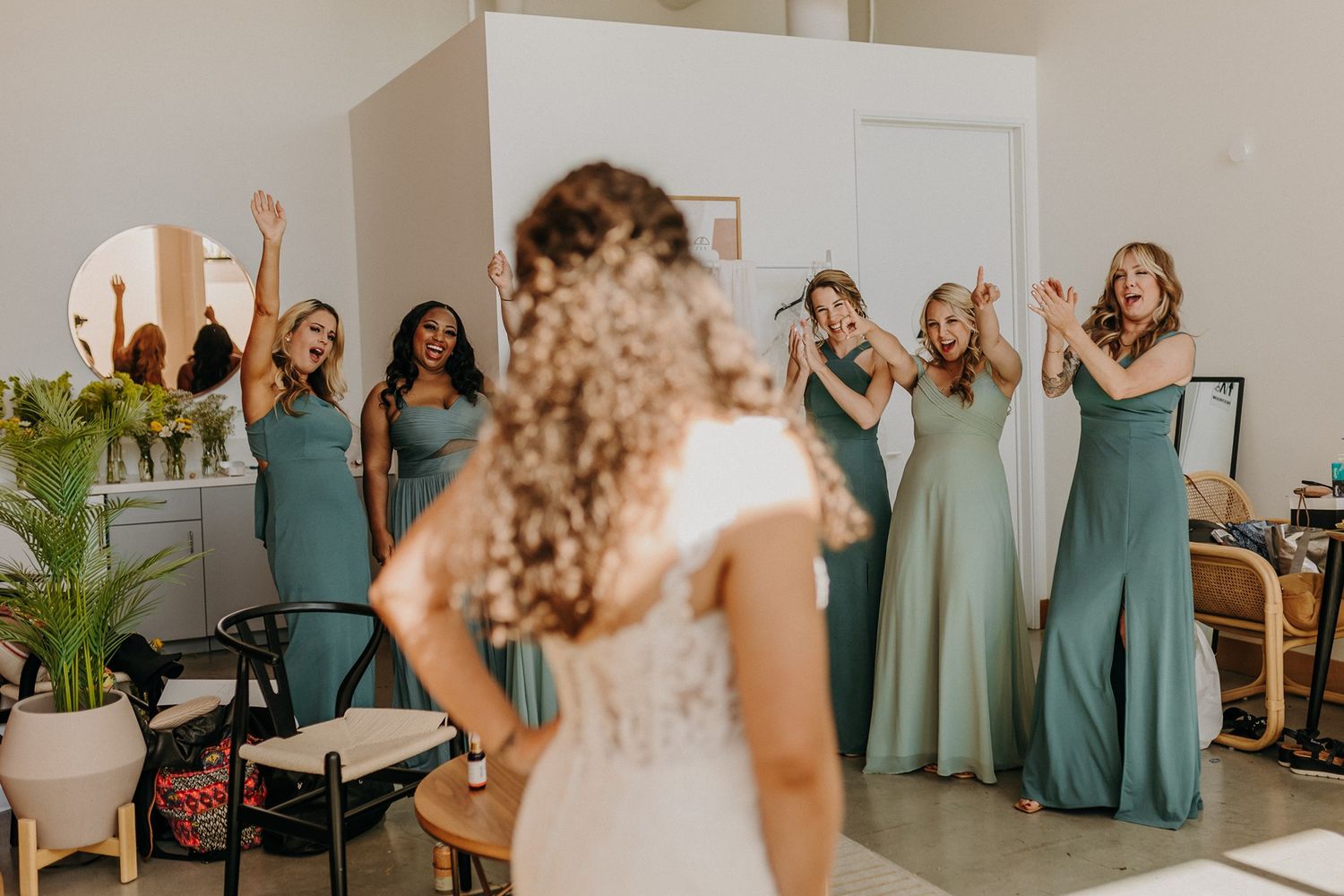 Bridesmaids in sage green gowns react with joy as bride reveals her wedding dress during bridal party preparations at The Lane.