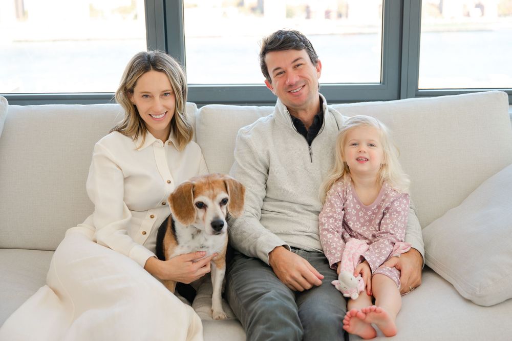 Happy family with a beagle dog sitting together on a white sofa in a bright living room.