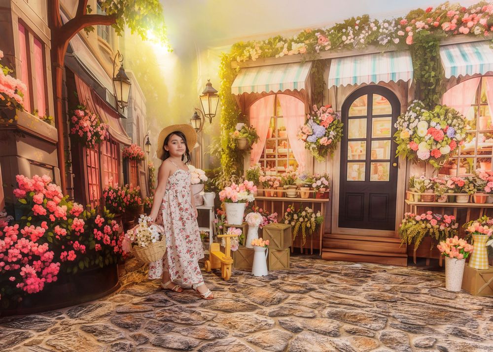Young girl in floral dress and hat poses in a picturesque flower market studio backdrop.