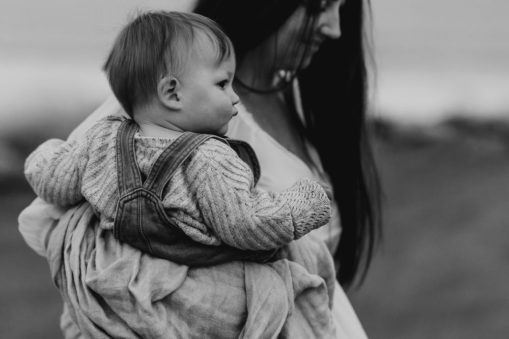 Black and white photo of a mother tenderly holding her baby in a cozy knit outfit outdoors.
