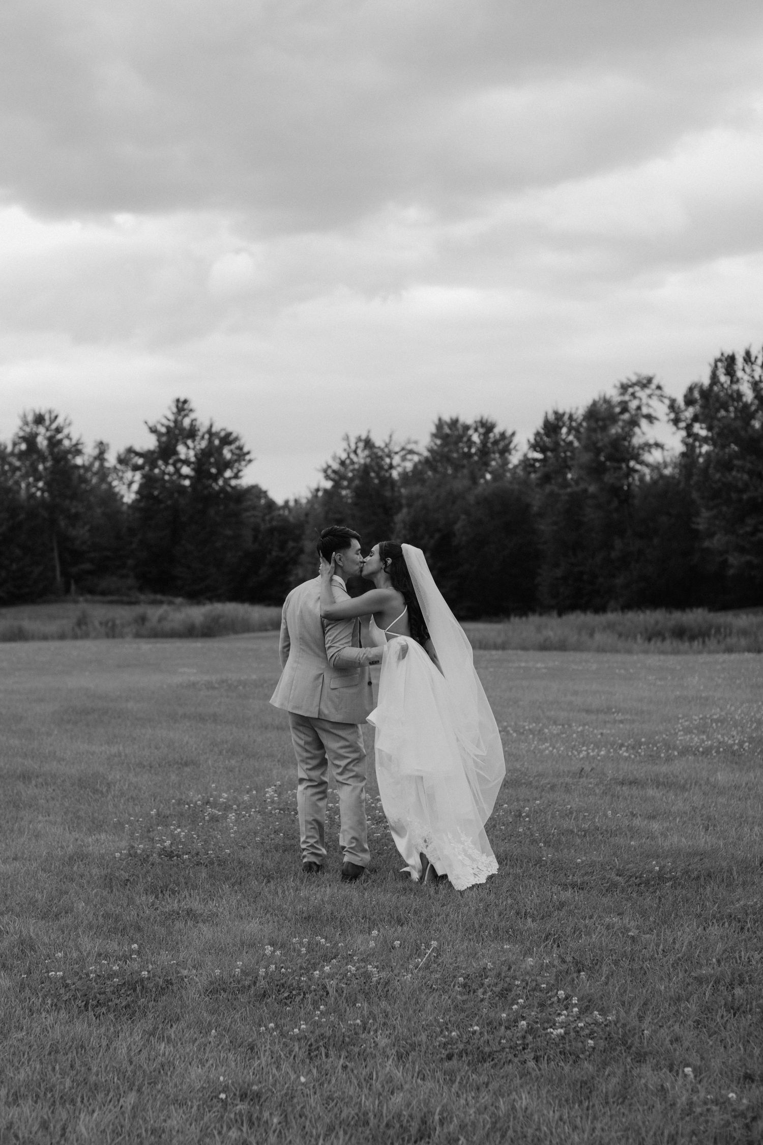 A romantic wedding moment captured in black and white on a grassy field.