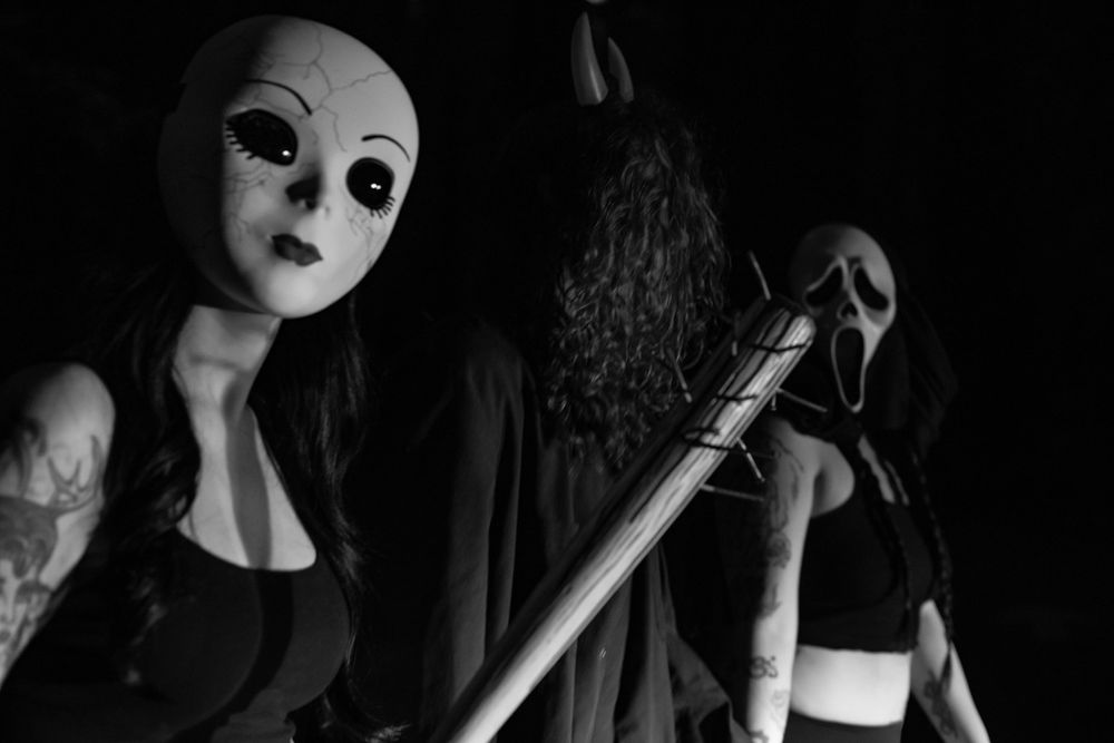 Creepy masked figures with white faces hold staffs in dark atmospheric lighting.
